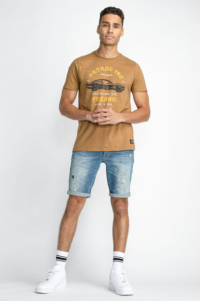 Jean short bleu de Petrol Industries, avec des détails froncés et des poches roulées, porté avec des baskets blanches et des chaussettes.