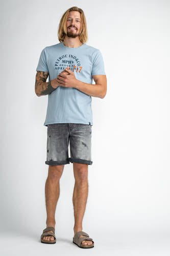 Jean short bleu marine de Petrol Industries, avec un lavage délavé et des jambes roulées, associé à un T-shirt bleu clair et des sandales en cuir de mouton.