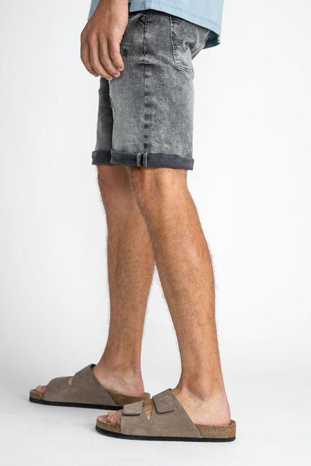 Short de denim bleu marine de Petrol Industries®, avec des poches rabattables, porté avec des sandales brunes.