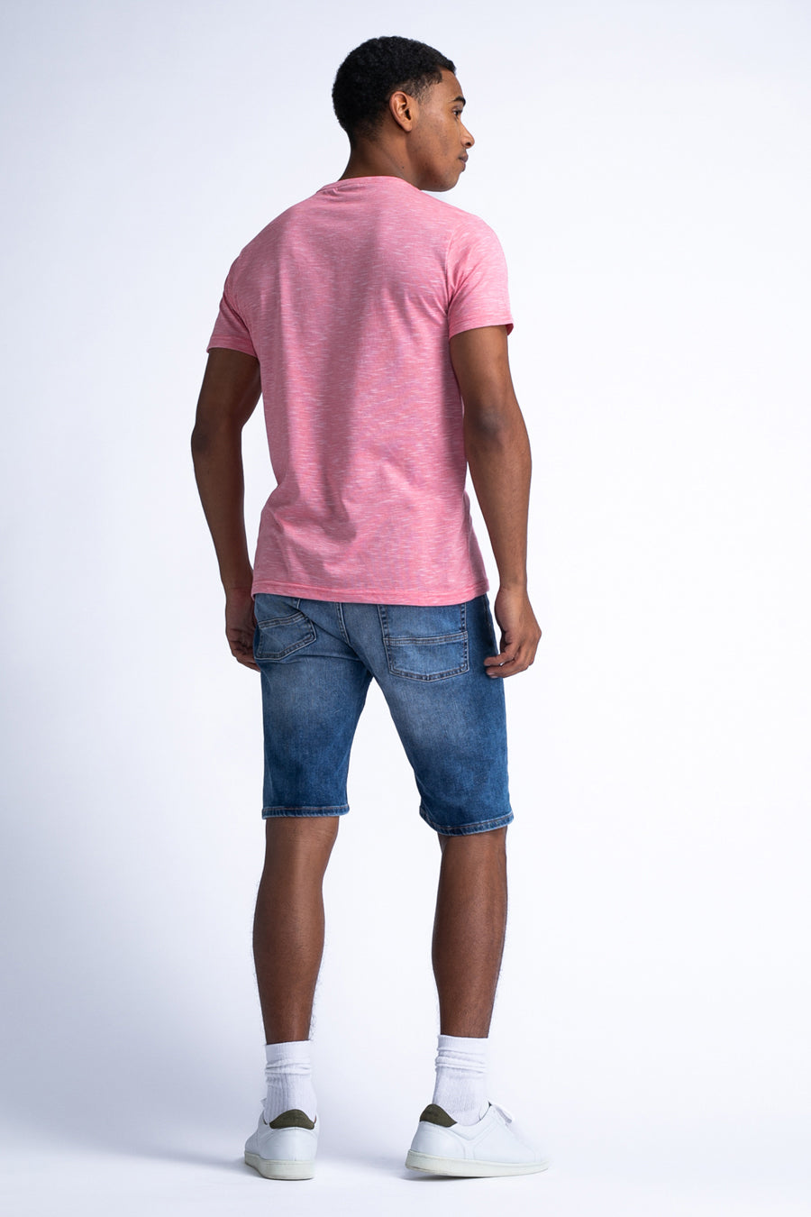 Man van achteren, roze shirt, blauwe denim short, witte sokken en schoenen.

