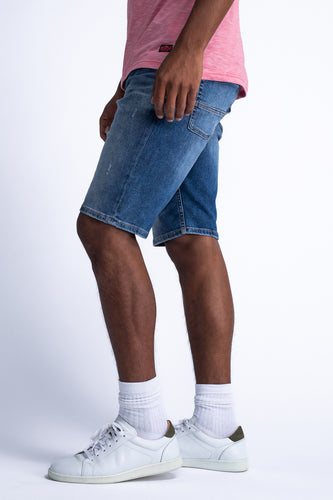 Man in roze shirt, jeans shorts, witte sokken en sneakers.