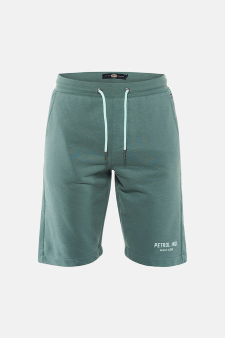 Shorts verts de Petrol Industries, avec cordon blanc et un logo de la marque sur la jambe, portés avec un t-shirt gris et des baskets.