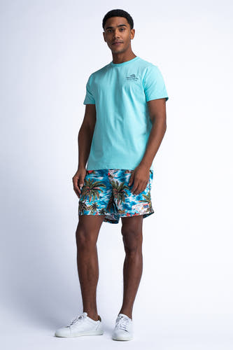 Short de natation bleu de Petrol Industries avec une impression frappante de palmiers et des baskets blanches.