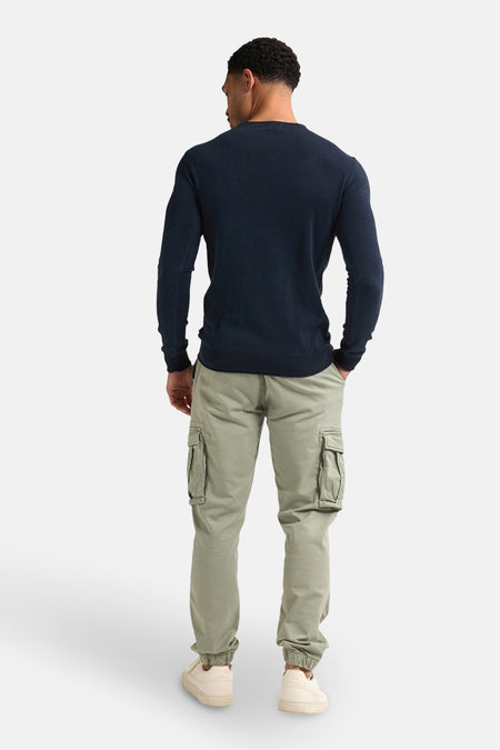 Blauwe trui met ronde hals van Petrol Industries, gezien van achteren, gecombineerd met cargo broek en crèmekleurige sneakers.