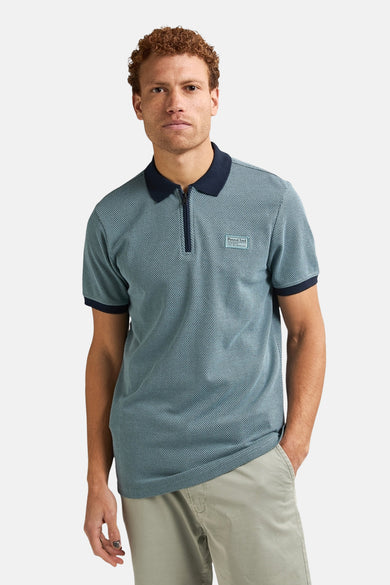 Man met blauw geruite polo shirt met korte rits en beige broek.