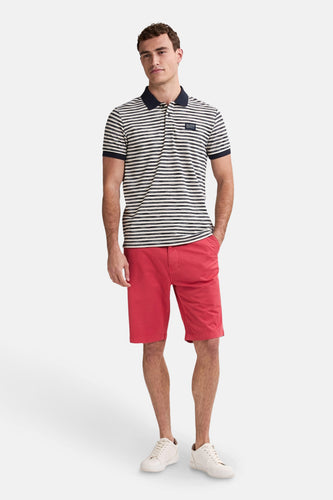 Een man in een gestreept poloshirt en rode korte broek, staand.