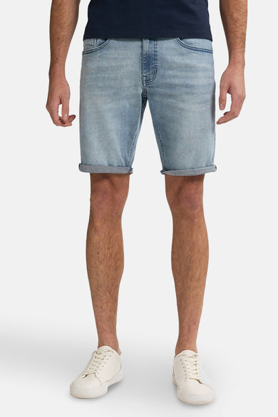 Lichtblauwe denim jeansshort van Petrol Industries, met opgerolde pijpen, gecombineerd met witte sneakers en een donkerblauw T-shirt.
