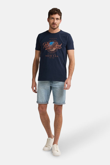 Lichtblauwe denim jeansshort van Petrol Industries®, gedragen met een donkerblauw T-shirt en witte sneakers.