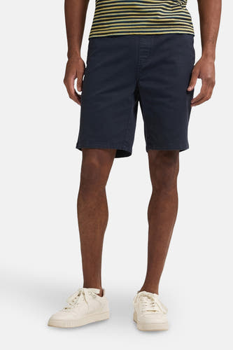 Blauwe short van Petrol Industries, met een elastische tailleband en gedragen met crèmekleurige sneakers en een gestreept shirt.
