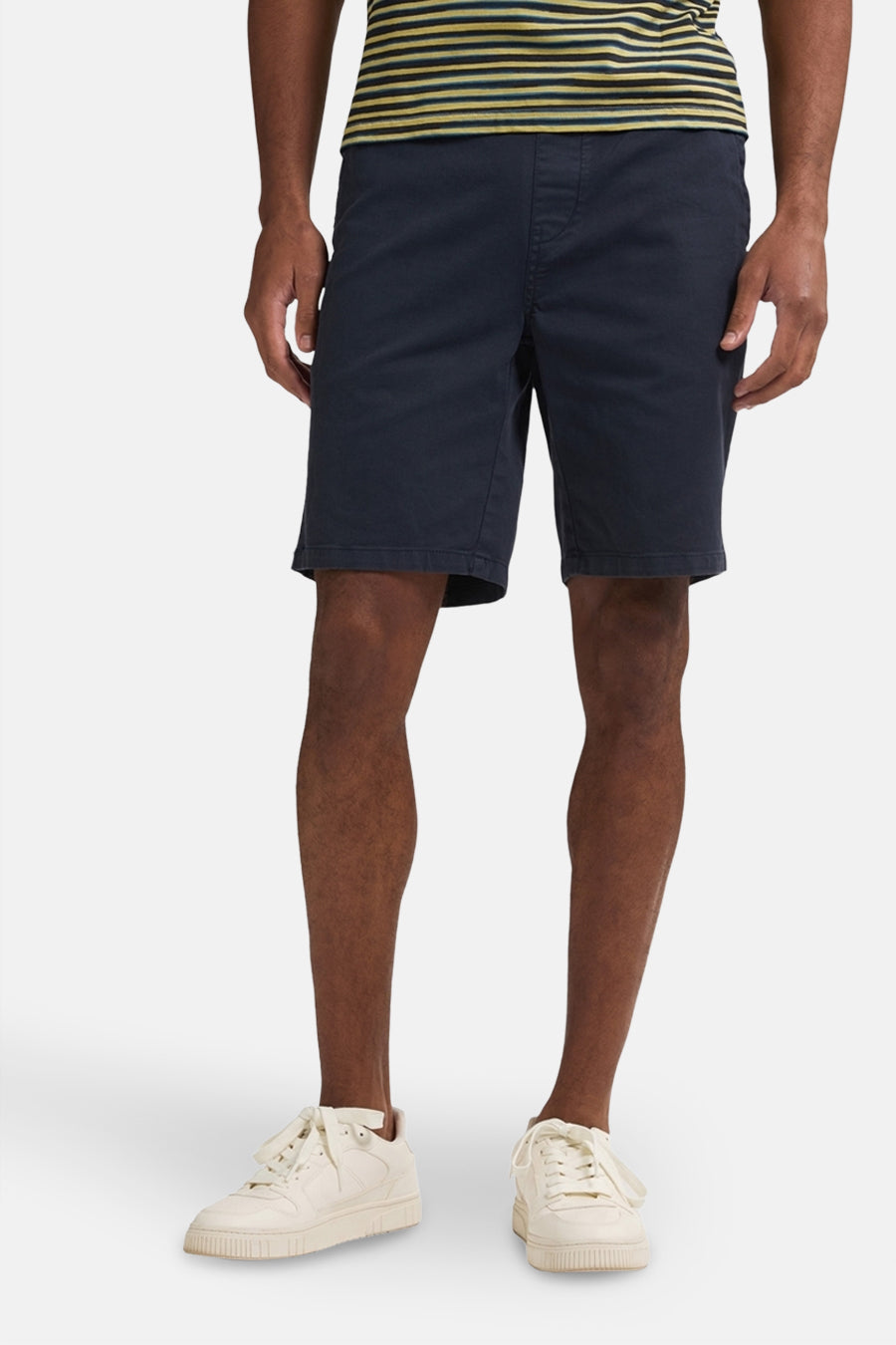 Blauwe short van Petrol Industries, met een elastische tailleband en gedragen met crèmekleurige sneakers en een gestreept shirt.
