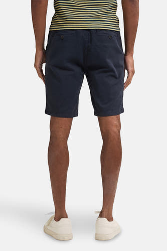 Blauwe short van Petrol Industries, met achterzakken, gedragen met een gestreept shirt en crèmekleurige schoenen.
