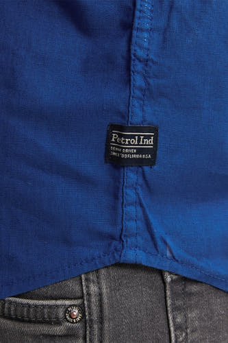 Chemise bleue à manches longues de Petrol Industries, gros plan sur l'étiquette et un pantalon gris.