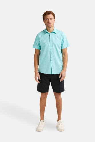 Chemise turquoise à manches courtes de Petrol Industries, portée avec des shorts noirs et des baskets crème.