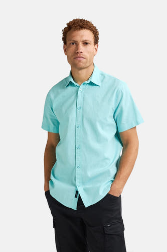 Chemise turquoise à manches courtes de Petrol Industries, avec col boutonné et portée avec une jupe noire.
