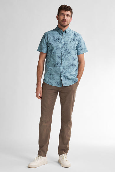 Chemise bleue à manches courtes de Petrol Industries, avec imprimé floral et associée à un pantalon marron et des baskets blanches.