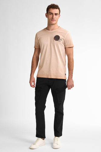 Man in beige t-shirt, zwarte cargobroek en witte sneakers.
