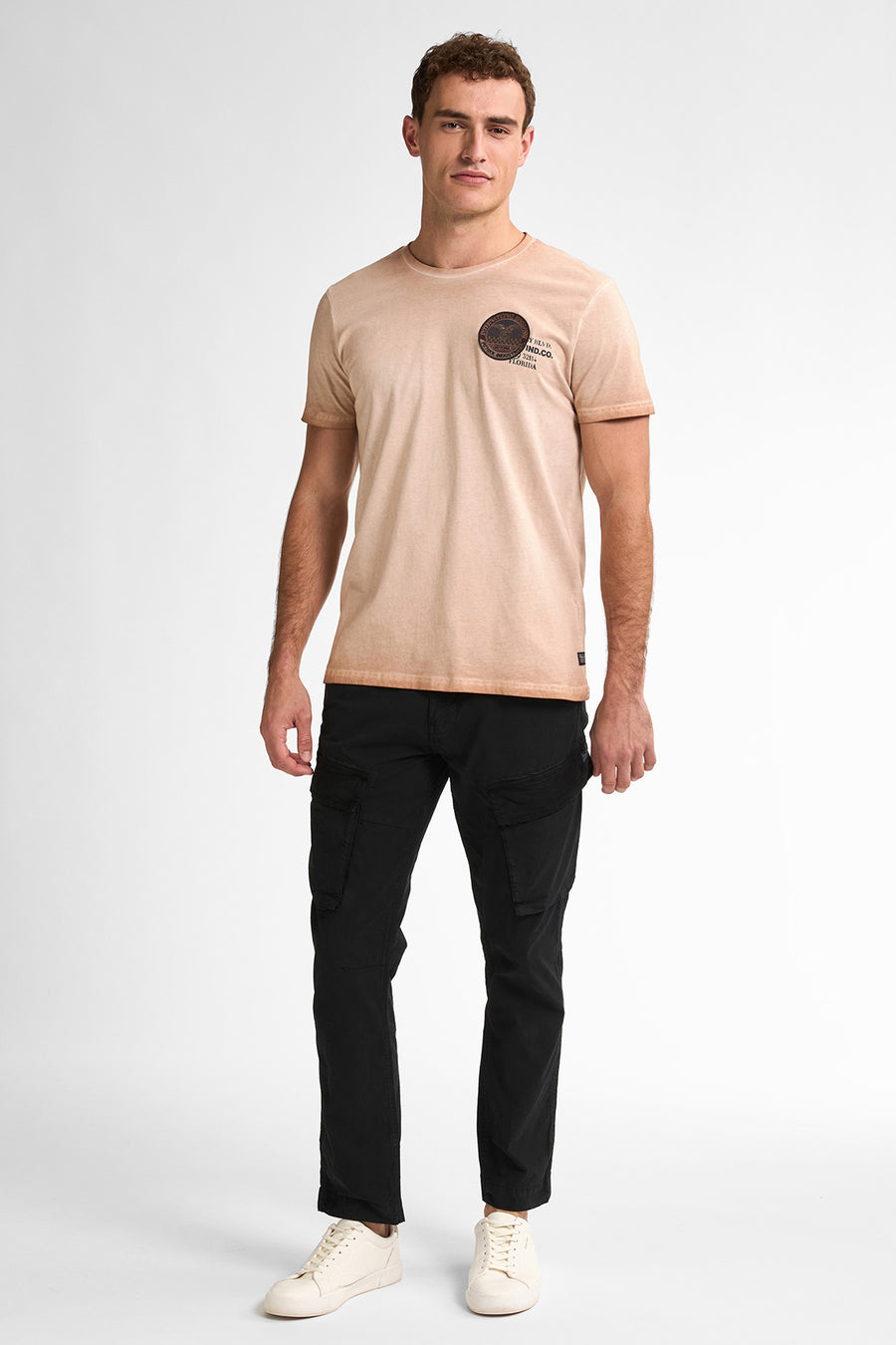 Man in beige t-shirt, zwarte cargobroek en witte sneakers.