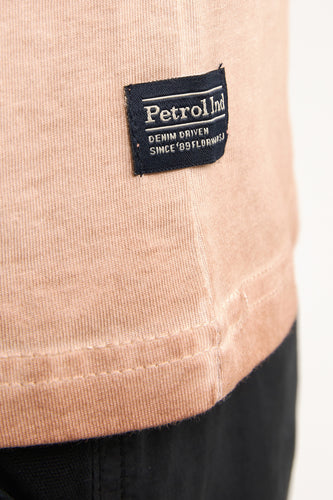 Close-up beige t-shirt met logo en zwarte broek.
