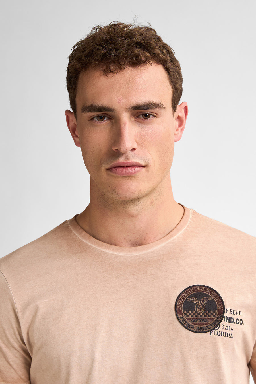 Portret van man in beige T-shirt met logo.