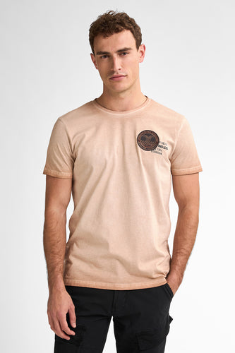 Man in beige T-shirt en zwarte broek, staand.
