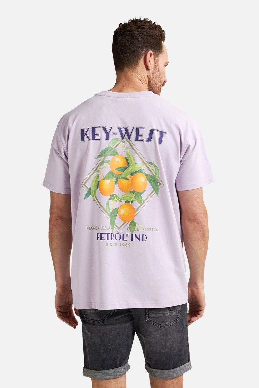 Man draagt lila T-shirt met oranje print en grijze spijkerbroekshorts.