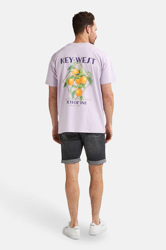 Een man van achteren gezien in een lila T-shirt met sinaasappeldruk, zwarte denim shorts en witte sneakers.