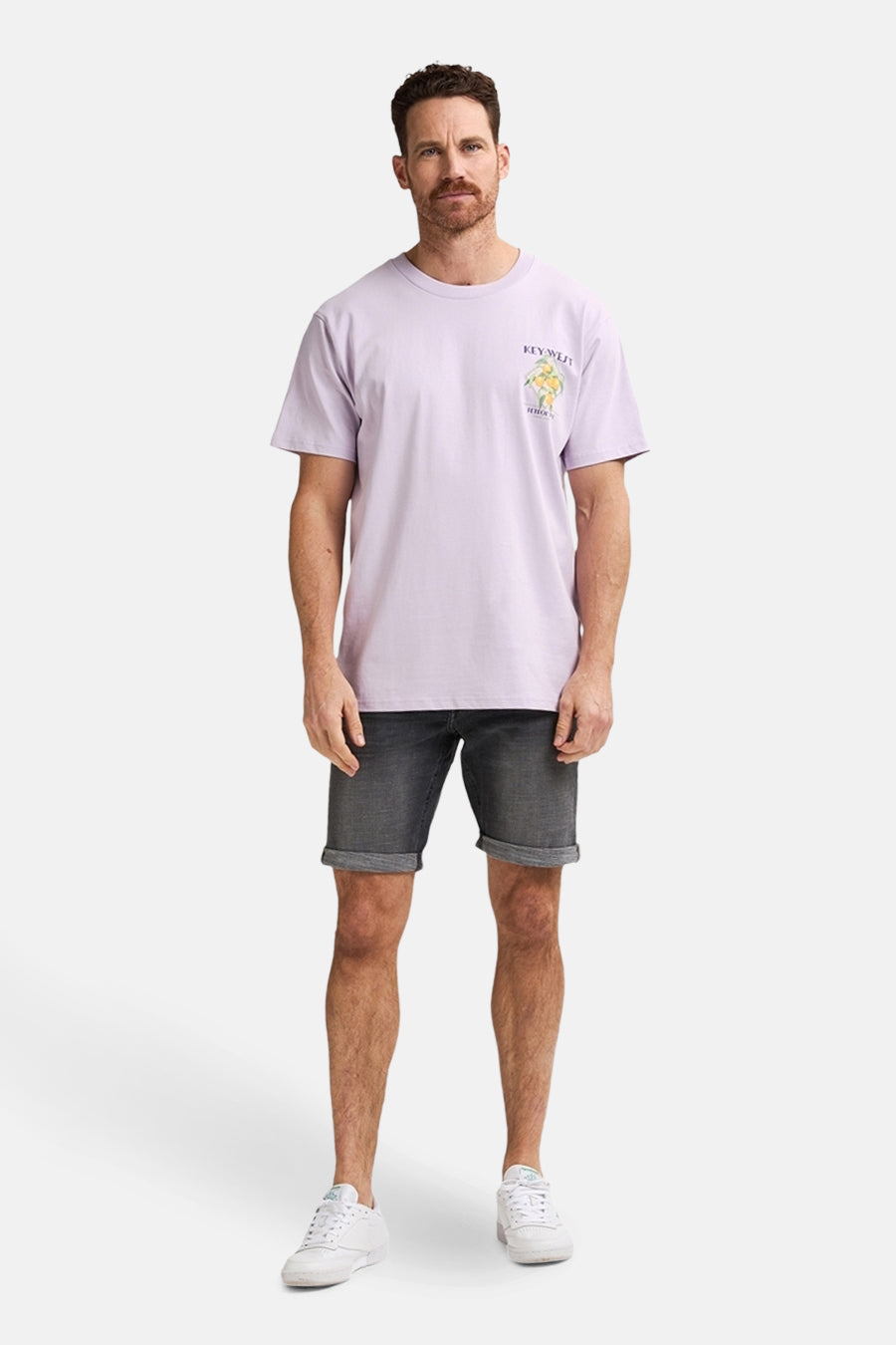 Man in lila T-shirt, grijze korte broek en witte sneakers.