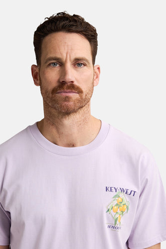 Een man draagt een lila T-shirt met Key-West print.