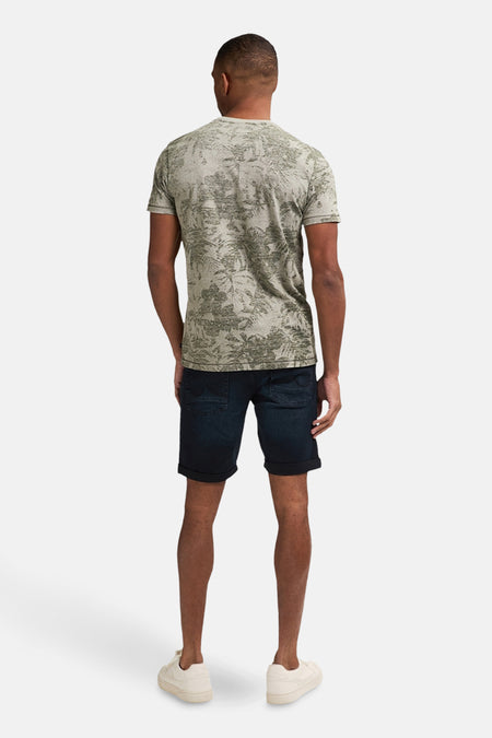 T-shirt vert avec manches courtes de Petrol Industries, avec un imprimé botanique, associé à des shorts en jeans et des baskets.
