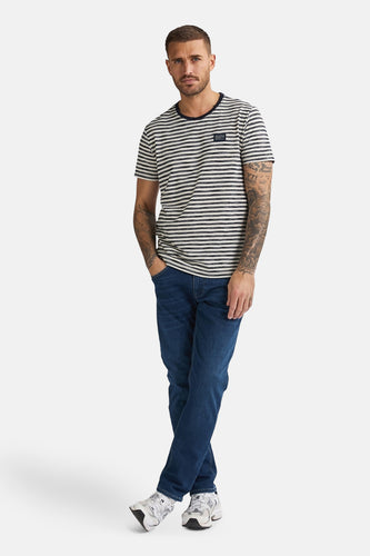 Man in gestreept shirt, jeans en sneakers op witte achtergrond.