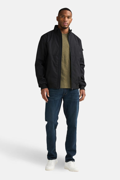 Veste courte noire de Petrol Industries®, combinée avec un t-shirt vert olive, un jean bleu foncé et des baskets blanches.