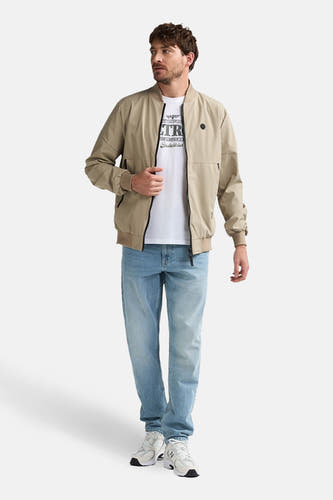 Veste courte beige de Petrol Industries®, avec fermeture éclair et portée avec un t-shirt blanc et un jean bleu.