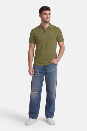 Groene polo van Petrol Industries met korte mouwen en een logopatch, gecombineerd met blauwe jeans en witte sneakers.