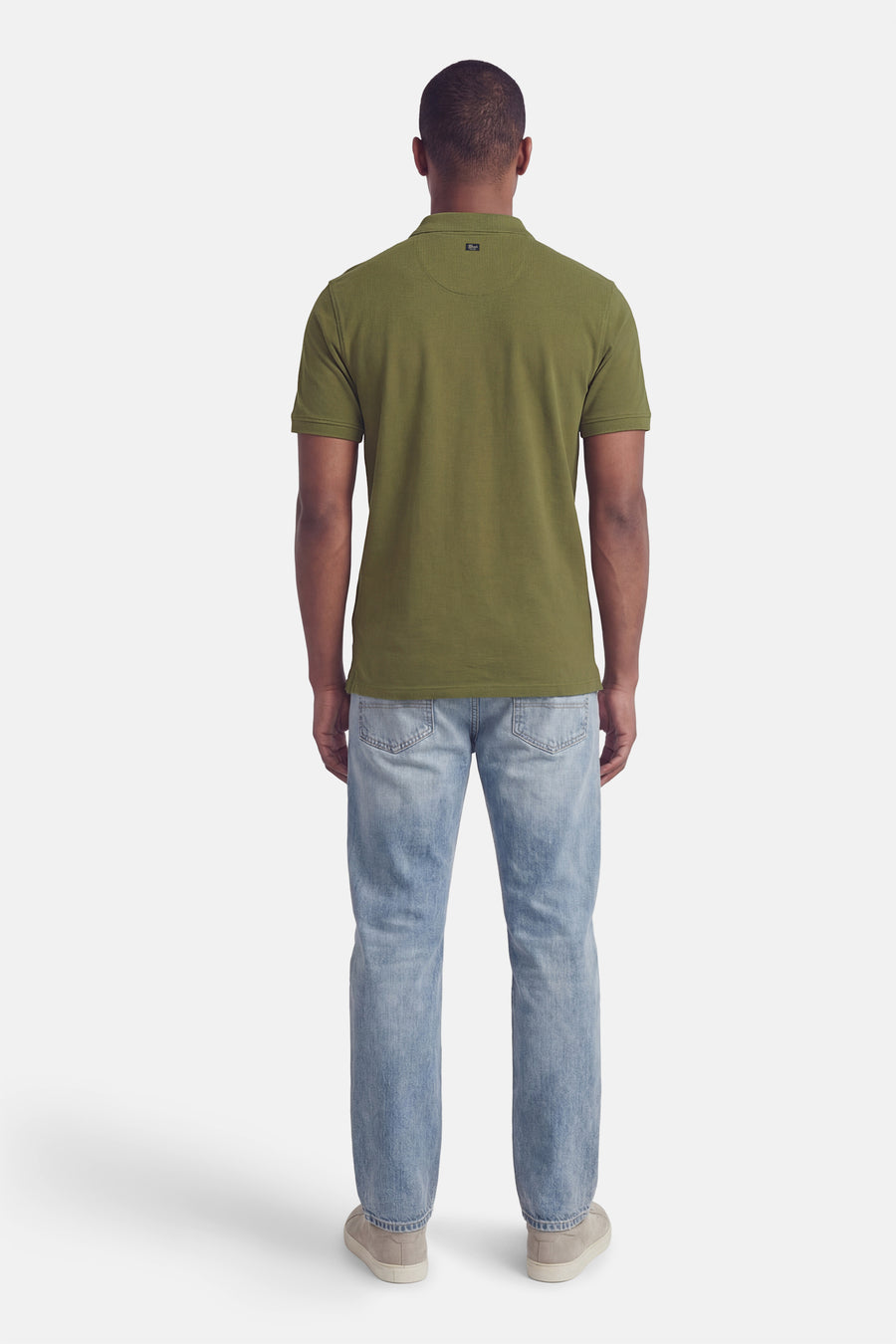 Polo verte à manches courtes de couleur verte de Petrol Industries, vue de dos, combinée avec un jean clair et des chaussures en daim.
