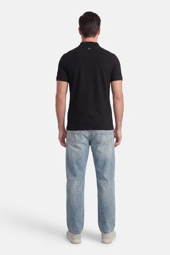 Polo noire à manches courtes de Petrol Industries®, portée avec un jean bleu clair et des baskets grises, vue de dos.