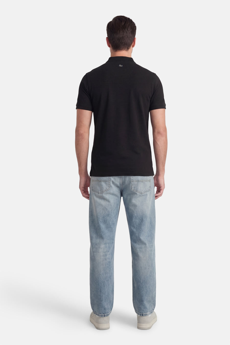 Polo noire à manches courtes de Petrol Industries®, portée avec un jean bleu clair et des baskets grises, vue de dos.