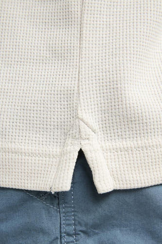 Polo écru de Petrol Industries® avec structure gaufrée et courte patte de boutonnage, portée sur un pantalon bleu.