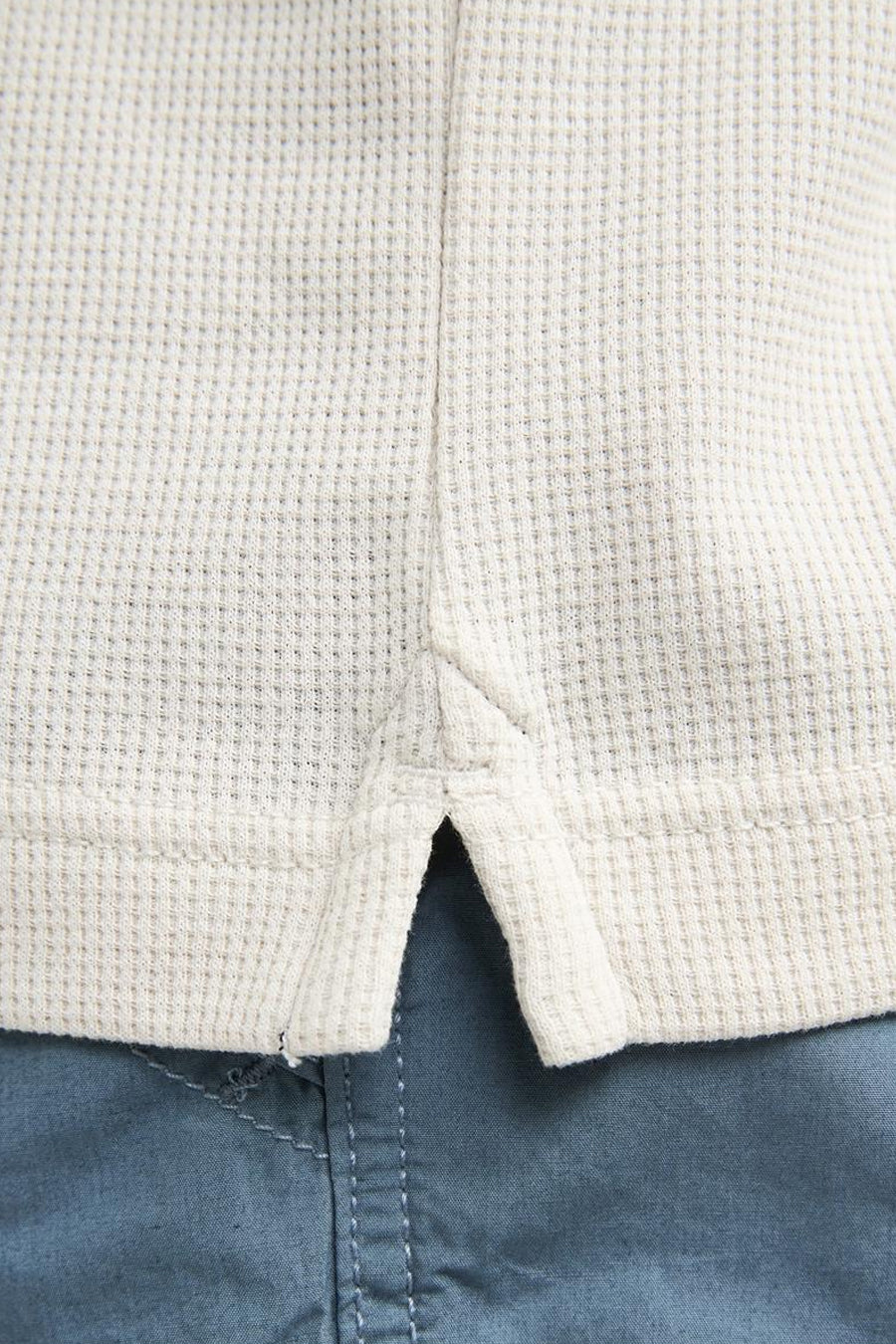Polo écru de Petrol Industries® avec structure gaufrée et courte patte de boutonnage, portée sur un pantalon bleu.