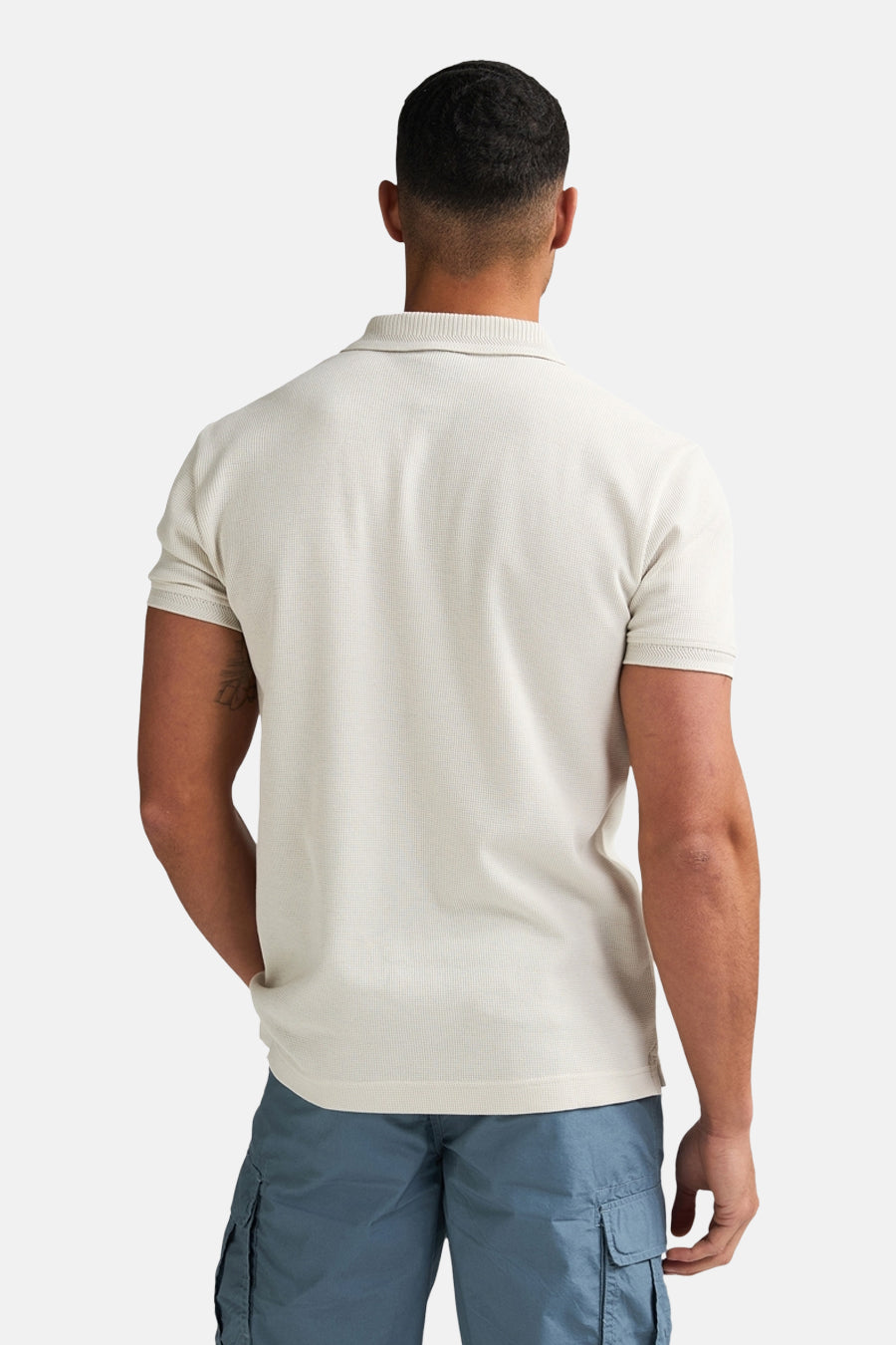 Polo écru à manches courtes de Petrol Industries, tissu uni et tatouage visible sur le bras.