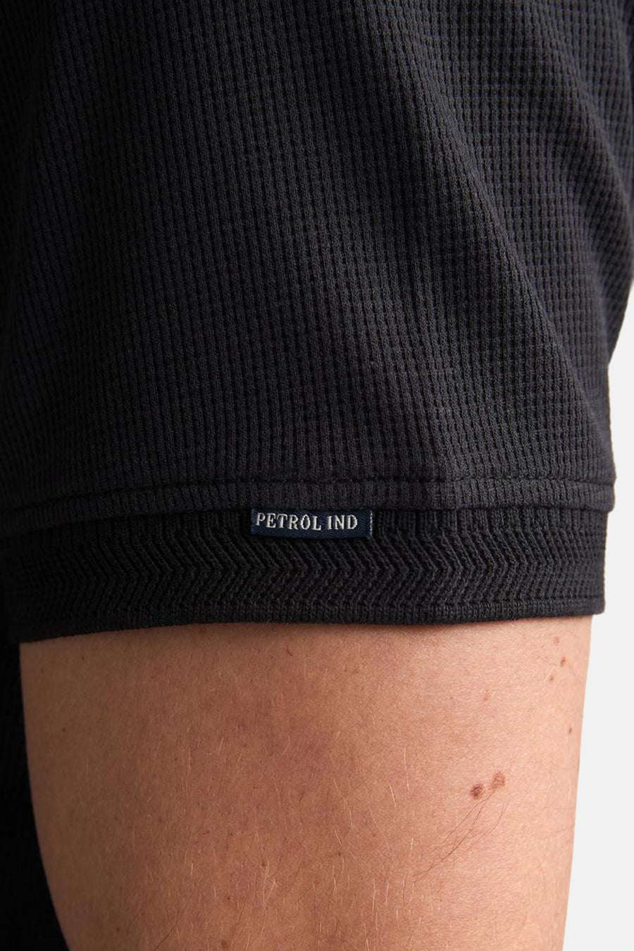 Polo noire Petrol Industries avec texture côtelée et détail de bordure tissée.