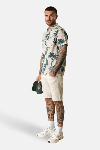 Chemise multicolore à manches courtes de Petrol Industries, avec un motif floral et portée avec des short blancs et des baskets.