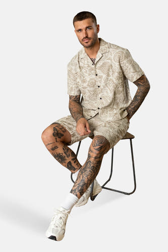 Chemise écru à manches courtes de Petrol Industries, avec motif paisley, portée avec des shorts coordonnés et des baskets blanches.