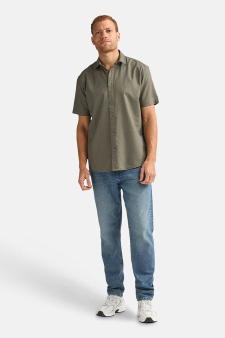 Chemise verte à manches courtes de Petrol Industries, associée à un jean bleu et des baskets blanches.