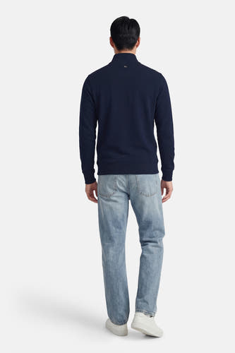 Pull bleu à col rond de Petrol Industries, vu de dos, avec un jean bleu clair et des baskets blanches.