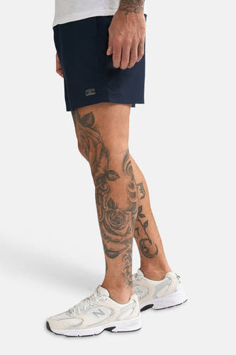 Short de bain bleu de Petrol Industries, avec jambes courtes et en plus un homme tatoué avec des chaussures blanches.