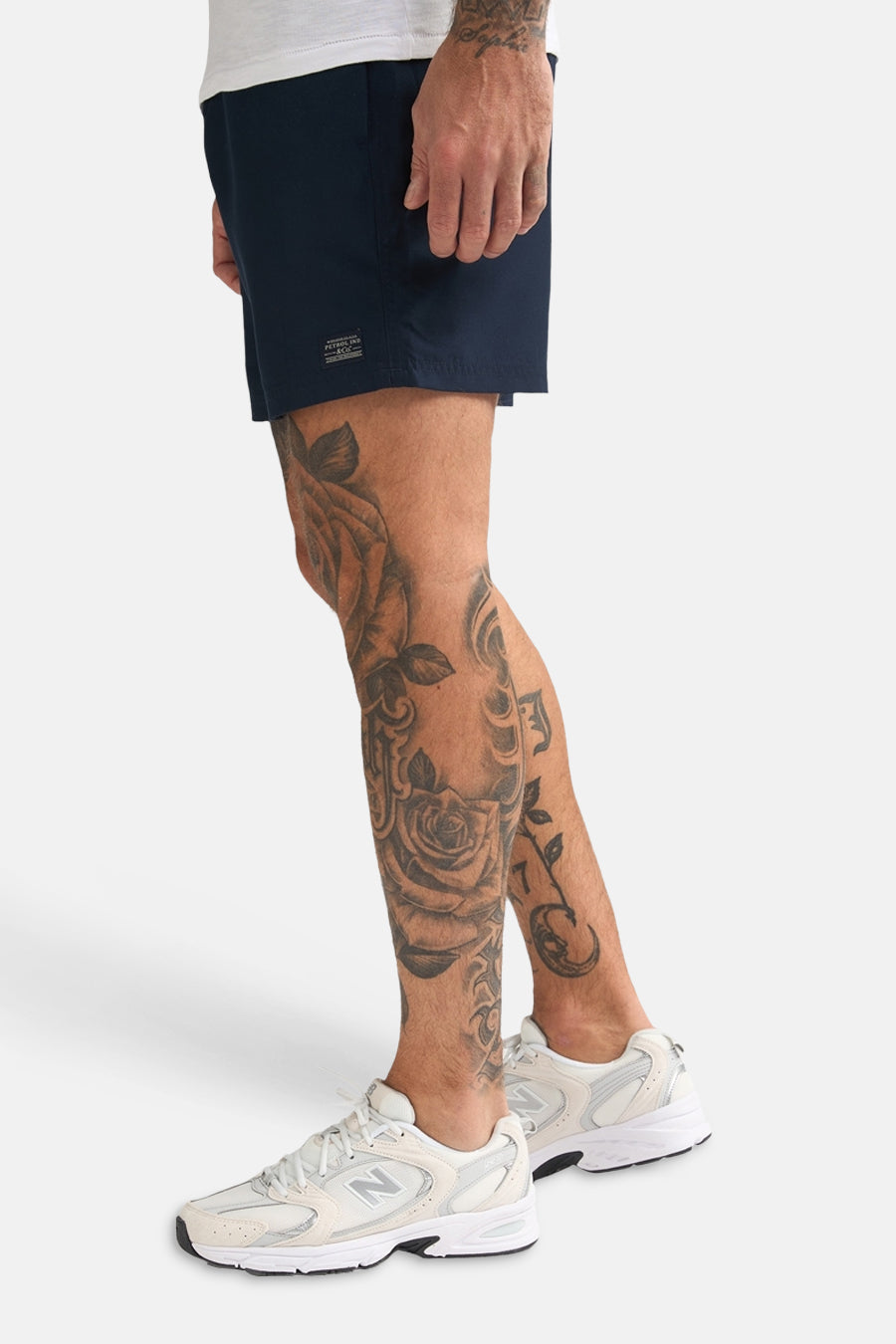 Short de bain bleu de Petrol Industries, avec jambes courtes et en plus un homme tatoué avec des chaussures blanches.