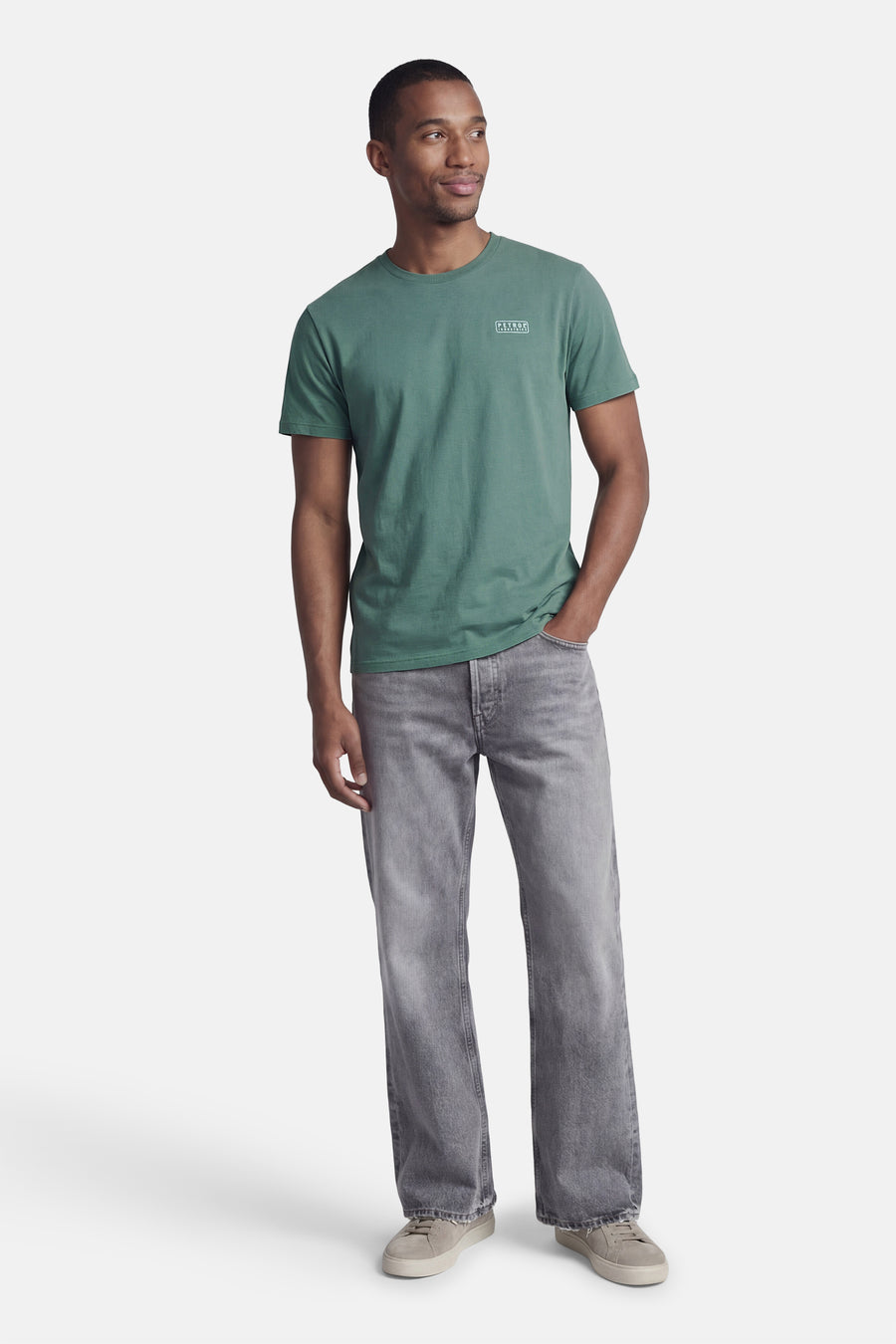 Groen T-shirt met korte mouwen van Petrol Industries, met een logo op de borst en gedragen met grijze jeans.
