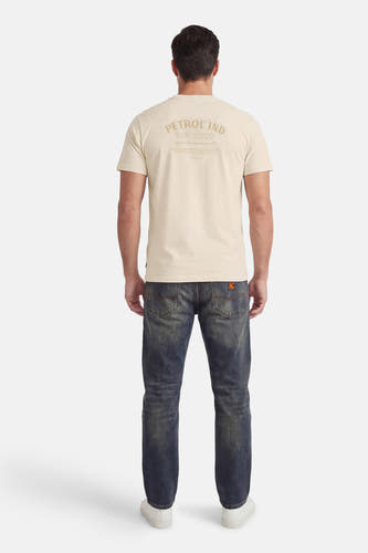 T-shirt écru à manches courtes de Petrol Industries, avec imprimé texte au dos, porté avec un jean et des baskets blanches.