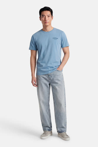 Blauw T-shirt met korte mouwen van Petrol Industries, met een kleine print op de borst, gedragen met een lichte jeans en grijze schoenen.
