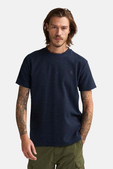 T-shirt bleu à manches courtes de Petrol Industries, vu de dos avec des manches tatouées et un pantalon kaki.